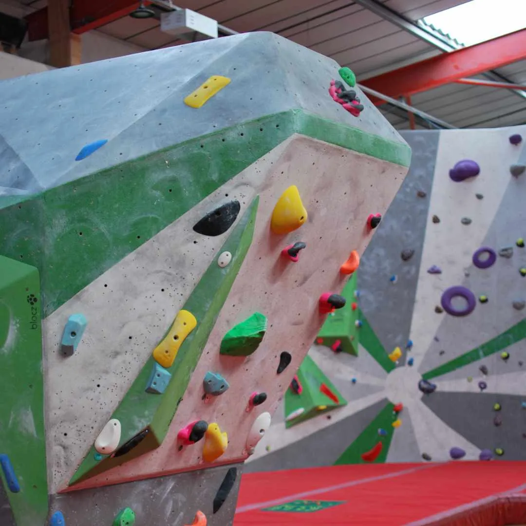 A grey slab wall set with green holds